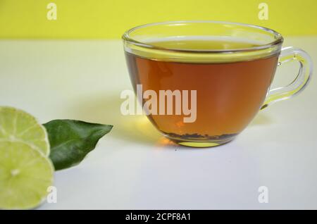 Tazzina trasparente e teiera con tè nero, tè secco sul tavolo, fette di bergamotto o limone o lime su sfondo bianco Foto Stock