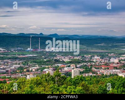 Vista dalla montagna al paesaggio con la città nella valle e la fabbrica con due alti camini dietro la città Foto Stock