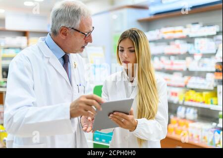 Due farmacisti parlano mentre lavorano su tablet nel loro negozio Foto Stock