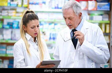 Due farmacisti parlano mentre lavorano su tablet nel loro negozio Foto Stock