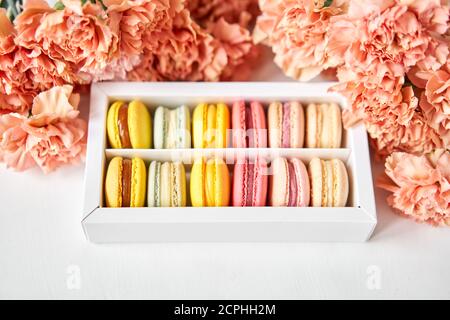 tondini bellissimi dolci macaroni in una scatola festiva con fiori su sfondo floreale. Ancora vita con torte di maccheroni e fiori diversi. Foto Stock