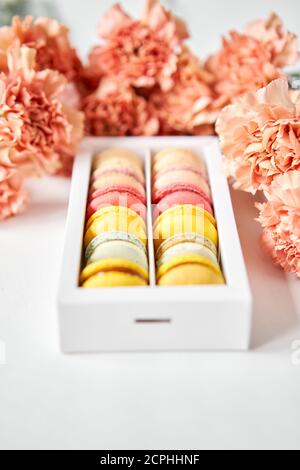 tondini bellissimi dolci macaroni in una scatola festiva con fiori su sfondo floreale. Ancora vita con torte di maccheroni e fiori diversi. Foto Stock