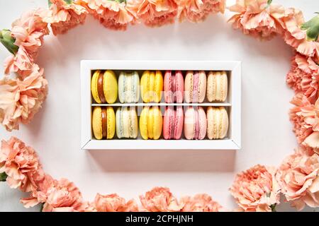 tondini bellissimi dolci macaroni in una scatola festiva con fiori su sfondo floreale. Ancora vita con torte di maccheroni e fiori diversi. Foto Stock