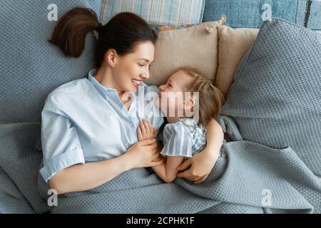 Una bella ragazza e sua madre godono di sole mattina. Buon tempo a casa. Il bambino si sveglia dal sonno. Famiglia che gioca sul letto in camera da letto. Foto Stock