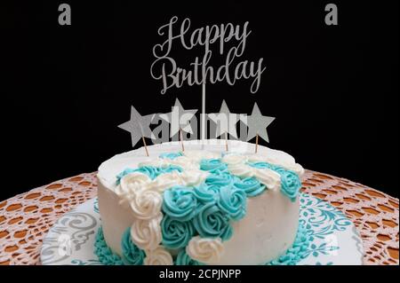 Torta di compleanno ricoperta di ghiaccio bianco e blu. Decorato con forme a stella e la frase: Buon compleanno. Isolato su sfondo nero. Vista frontale. Foto Stock