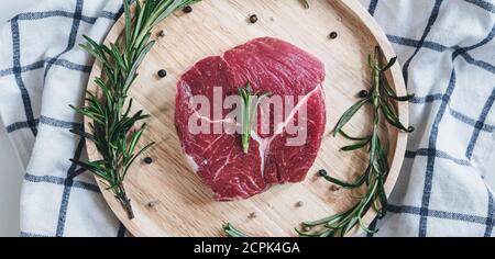 Carne cruda, bistecca di manzo, su tavola di legno con rosmarino Foto Stock