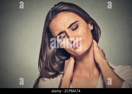 Malattia della schiena e della colonna vertebrale. Closeup ritratto donna stanca massaggiando il suo collo doloroso isolato su sfondo grigio parete. Espressione della faccia Foto Stock