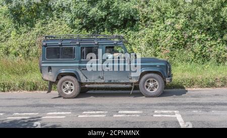 Land Rover Defender 4WD verde passando incrocio stradale. Non si è sicuri se si tratta di 110 da circa 2012-2015, il modello 127/130 più lungo, o il tipo di station wagon TD5 Foto Stock