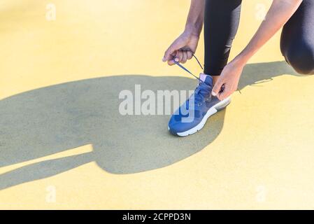 mani di una donna caucasica legando le sue scarpe blu e proiettando un'ombra su un pavimento giallo. copia spazio Foto Stock