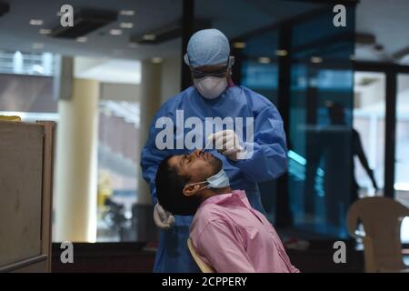 Un operatore sanitario raccoglie i campioni di tampone di un lavoratore dell'autorità municipale in uno speciale campo di test, a Nuova Delhi, India. Un record 95,880 coro Foto Stock