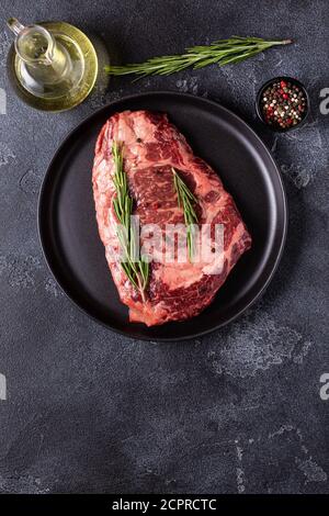 Bistecca di manzo fresco crudo su piatto nero, vista dall'alto. Foto Stock