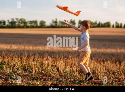 Happy child corre con un aeroplano giocattolo su uno sfondo tramonto su un campo. Il concetto di una famiglia felice. Sogni d'infanzia Foto Stock