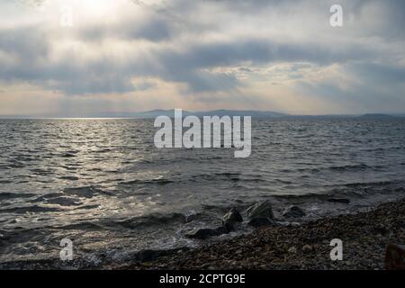 Alberi di luce solare che brillano attraverso le nuvole al mare Foto Stock