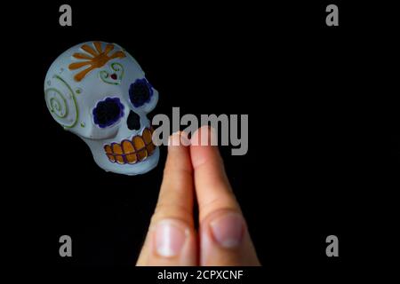 Mani di un uomo che prega ad una testa cranica di il giorno dei morti dipinta a mano su un sfondo nero Foto Stock