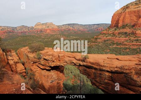 Una valle piena di sempreverdi e arenaria rossa con bianche montagne calcaree sullo sfondo del Ponte del Diavolo a Sedona, Arizona, USA Foto Stock