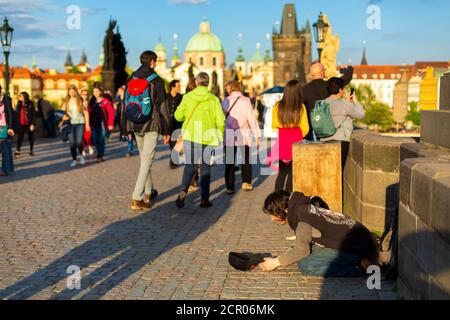 Un ragazzo in ginocchio chiede elemosina ai passanti sul ponte Carlo di Praga. Foto Stock