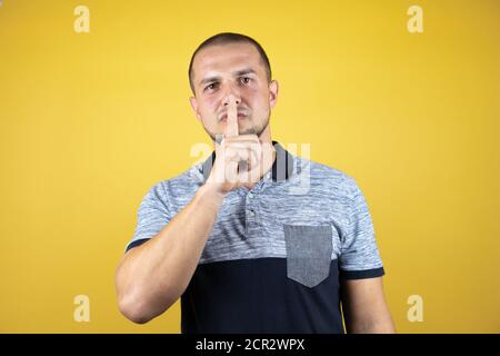 Uomo russo in piedi su sfondo giallo insolato chiedendo di essere tranquillo con il dito sulle labbra. Silenzio e concetto segreto. Foto Stock