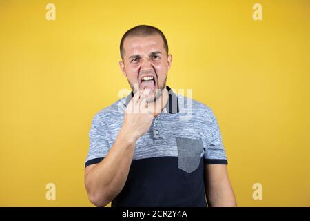 L'uomo russo in piedi su sfondo giallo insolato disgustato con lei mano dentro la bocca Foto Stock