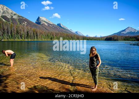 La scena estiva del Lago di Luna di Miele con una donna in piedi nel lago e godendo la vista delle montagne circostanti nel Parco Nazionale di Jasper, A. Foto Stock