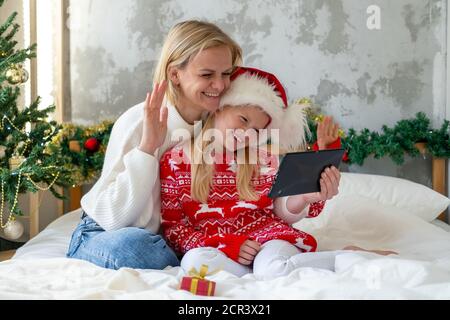 Natale online famiglia Complimenti. Sorridente madre bionda europea e figlia che usa un tablet mobile per videochiamare amici e genitori Foto Stock
