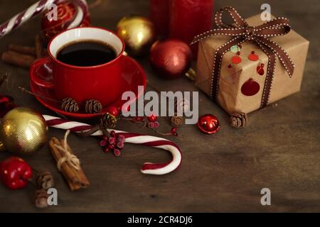 Addobbations.Red Cup di Natale con caffè, confezione regalo, caramelle di Natale, palle, coni e cannella su sfondo di legno, fuoco selettivo. Natale A. Foto Stock