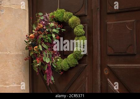 Corona con le bacche rosse e le foglie secche appese su una porta. Foto Stock