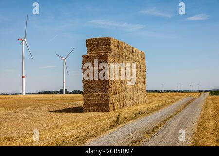 Linnich, Renania Settentrionale-Vestfalia, Germania - balle di paglia impilate sul campo stoppie dopo il raccolto di grano, dietro turbine eoliche nel parco eolico. Foto Stock