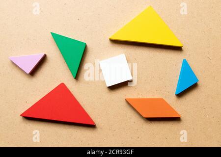 Puzzle tangram colore in pezzo che aspettano di completare la forma su sfondo di legno Foto Stock