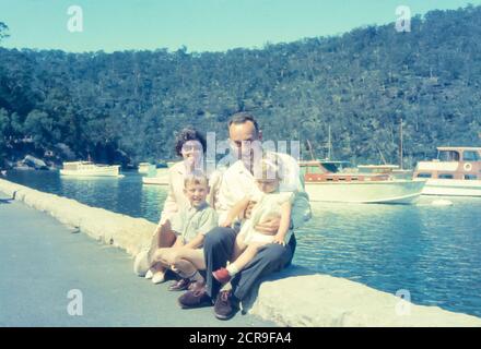 Bobbin Head, Sydney Australia 1965: Con belle barche in legno ormeggiate sullo sfondo una giovane famiglia australiana posa per una foto vicino al bordo delle acque a Bobbin Head nel Kuring-Gai National Park, Sydney, Australia Foto Stock