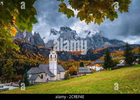Incredibile scenario autunnale con colorata foresta di larici. Affascinante villaggio alpino con bella chiesa. Grandi escursioni e luoghi turistici, Colfosco, Dolomiti Foto Stock