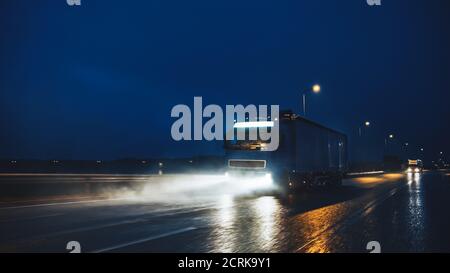 Blue Long Haul semi-Truck con Cargo Trailer Full of Goods viaggia di notte sulla Freeway Road, guidando attraverso il Continente attraverso pioggia, nebbia, neve Foto Stock