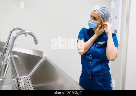 Il chirurgo femminile mette sulla maschera, preparandosi per l'intervento chirurgico Foto Stock