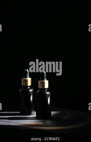 Pipettare il flacone contagocce in vetro nero con elementi dorati sul sfondo scuro Foto Stock