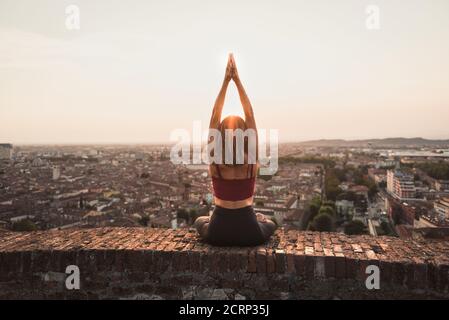 Vista frontale di una luce posteriore di una donna fedele in posizione yoga tenendo il sole al tramonto o all'alba in una splendida posizione in città con un caldo backgrou Foto Stock