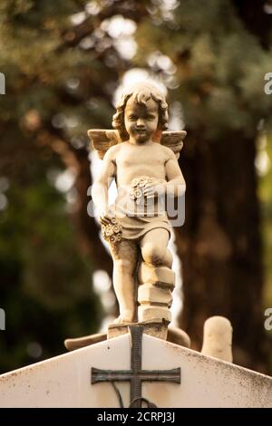 Piccola statua di un piccolo angelo ragazzo con le ali alla lapide presso il vecchio cimitero in Dalmazia, Croazia, primo piano sulla luce del sole Foto Stock