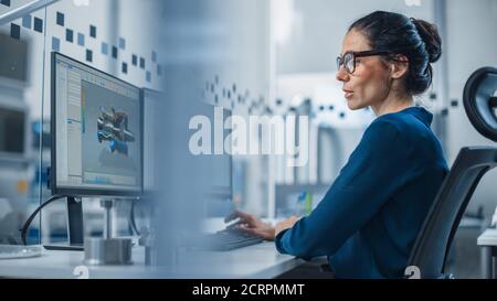 Industrial Female Engineer lavorando su un personal computer, due schermi di monitor mostrano il software CAD con prototipo 3D del nuovo motore ibrido a idrogeno e. Foto Stock