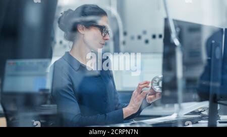 Sparato attraverso il vetro. Ingegnere femminile che lavora su Personal computer, modello di ispezione del meccanismo di macchine industriali. Lavora in ufficio, cioè Foto Stock