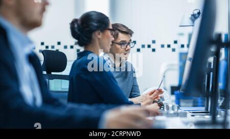 Fabbrica moderna: Il tecnico industriale maschile spiega al supervisore del progetto femminile le funzioni della parte macchina confrontandole con una sullo schermo del computer Foto Stock