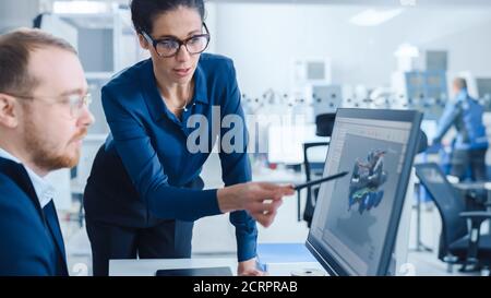 Modern Factory: La Supervisore del progetto femminile parla con un ingegnere industriale maschile che lavora su Personal computer. Utilizzano il software CAD per la progettazione e. Foto Stock