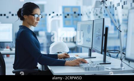 Bella ingegnere femminile che lavora su Personal computer nella High-Tech Industrial Factory, utilizza il software CAD per modellare l'High Tech dell'industria pesante Foto Stock