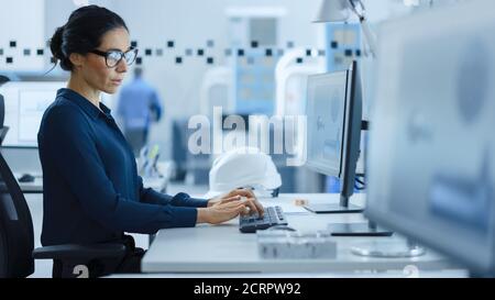 Bella ingegnere femminile che lavora su Personal computer nella High-Tech Industrial Factory, utilizza il software CAD per modellare l'High Tech dell'industria pesante Foto Stock