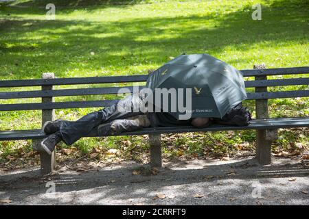 L'uomo dorme su una panchina sotto un ombrello a Central Park, New York City. Foto Stock