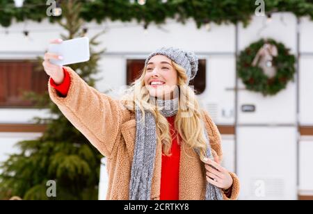 Bella donna che prende selfie su smartphone all'aperto, godendo di giornata invernale al campeggio Foto Stock