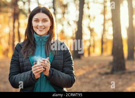 Donna allegra che tiene la tazza con il tè, che si riscalda alla foresta Foto Stock
