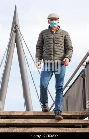 Uomo maturo con maschera facciale che cammina su un ponte pedonale una città - fuoco sull'uomo Foto Stock
