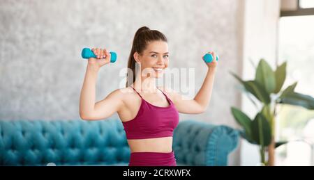 Allenamento domestico. Giovane donna atletica in allenamento sportivo con manubri interni Foto Stock