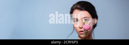 colpo panoramico di donna che copre l'occhio con fiori in polietilene isolato su blu, concetto di ecologia Foto Stock