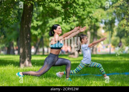 Le ragazze stanno excercising nel parco. Si stanno allungando insieme. Mamma e figlia. Vista laterale. Foto Stock