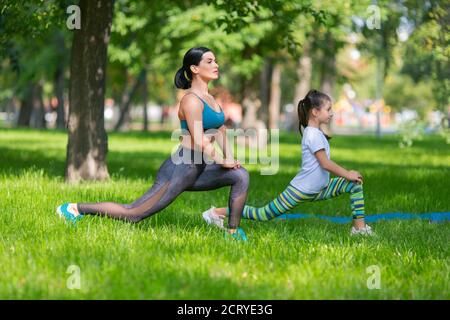 Le ragazze stanno excercising nel parco. Si stanno allungando insieme. Mamma e figlia. Vista laterale. Foto Stock