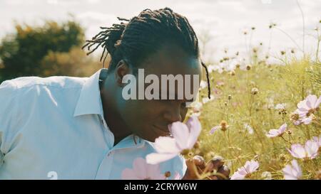 Bel giovane agricoltore africano che annuisce fiori viola in azienda. Foto di alta qualità Foto Stock